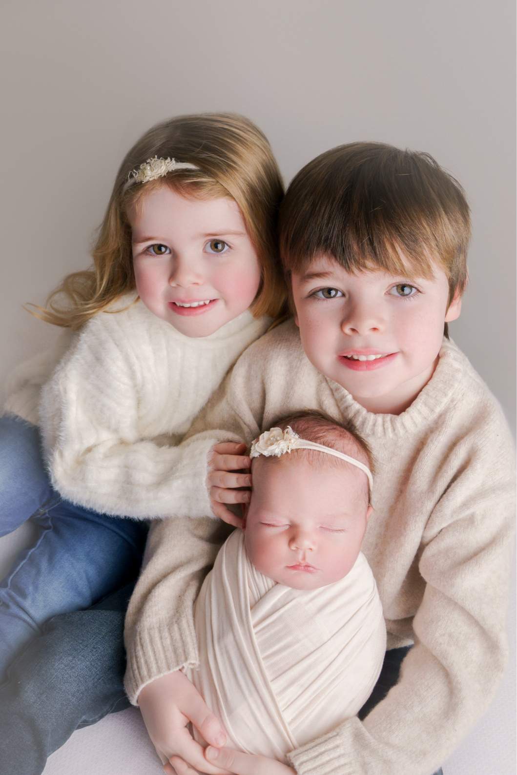 A girl and a boy holding their newborn baby sister lovingly