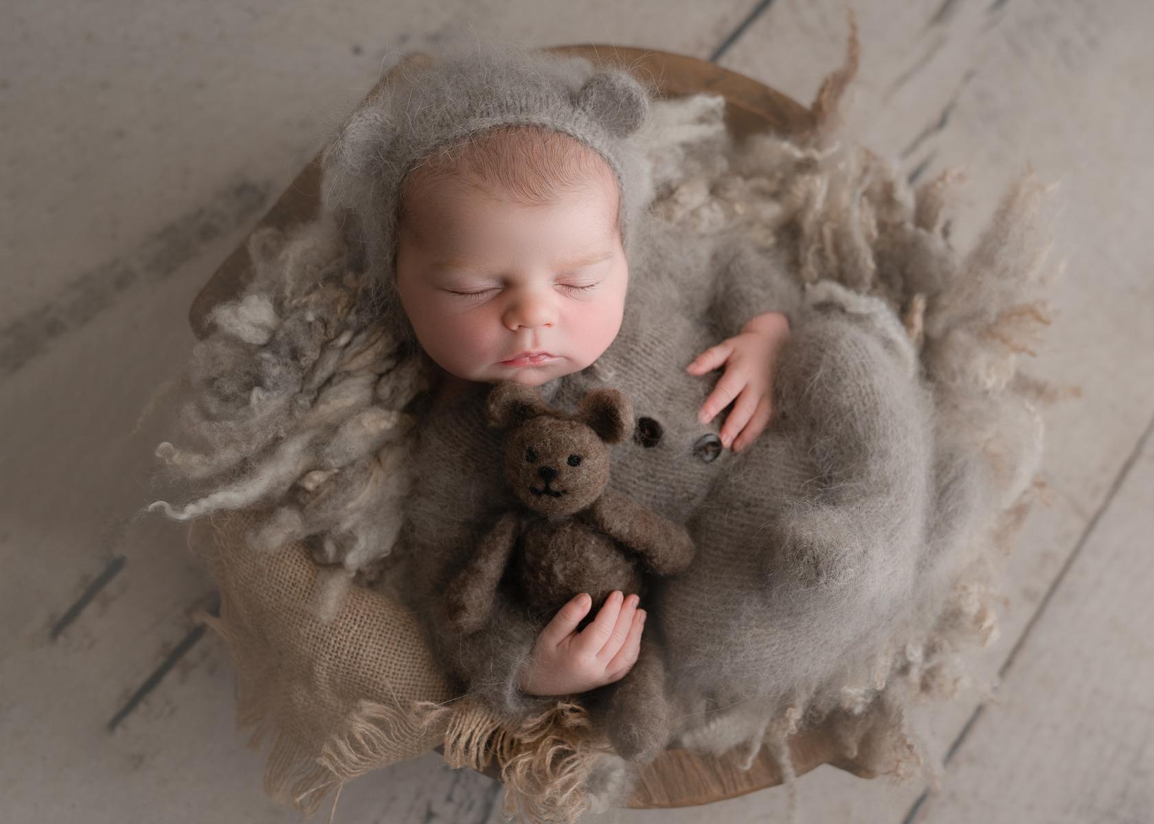 Newborn baby boy dressed in brown wool bear hat, wrapped in brown wool, holding a tiny bear, captured by Céire Rhein, Dublin's newborn photographer."