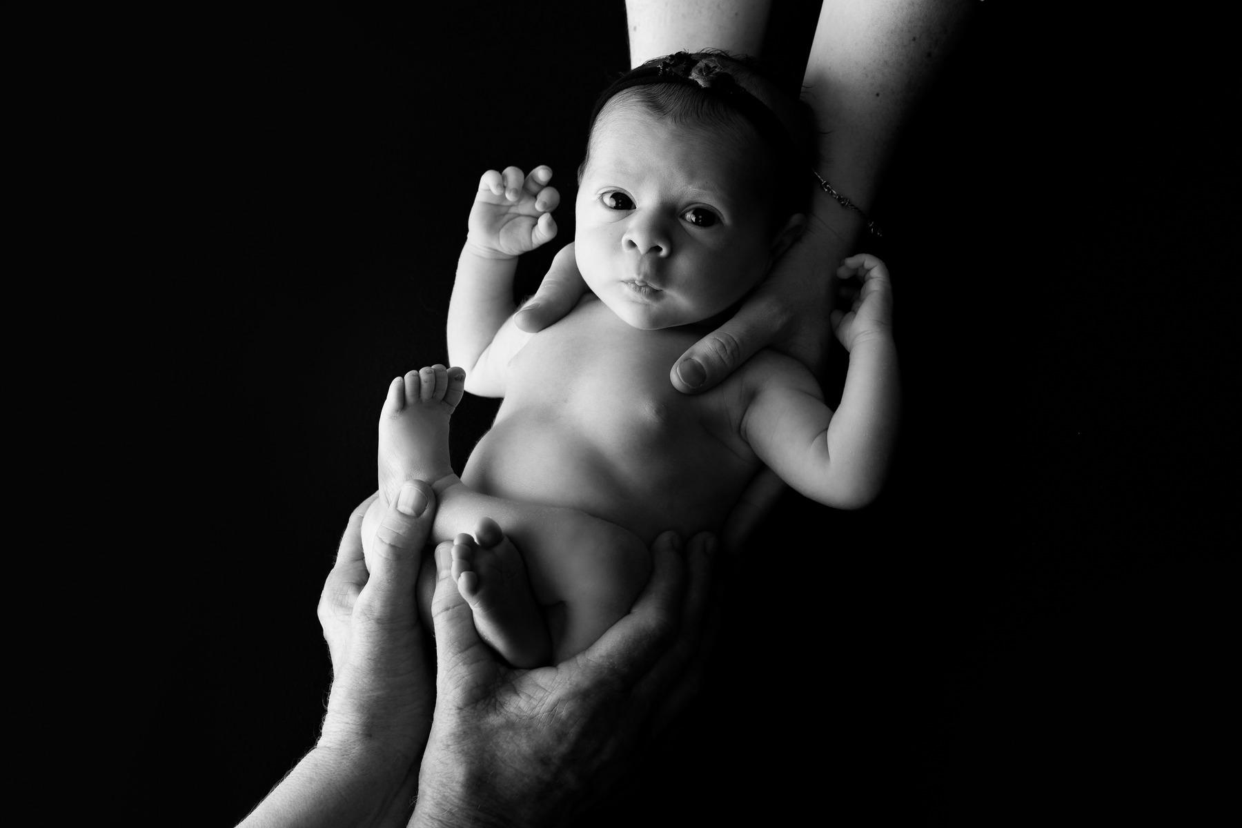 "Baby girl in black and white with parents' hands gently cradling her, captured by Céire Rhein, Dublin's newborn photographer."
